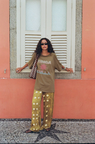 Relaxed-fit Kinga Csilla Sunset Tee in a sun-washed olive green, featuring a central sunset graphic with a coral and sky blue gradient.