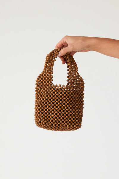 A studio shot featuring a person’s hand holding the walnut beaded bucket bag by its integrated top handle against a crisp white background, offering a direct sense of scale for the compact evening accessory.
