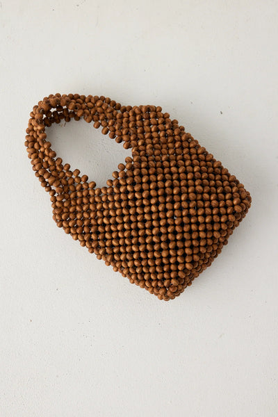 A direct overhead flat lay of the walnut brown beaded purse resting on a clean white surface, showcasing the tight, unlined geometric grid structure of the 100% wooden beads.