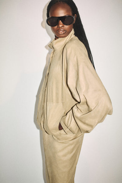 Editorial side close-up of a model wearing the Shona Joy Ernest sand faux suede funnel neck bomber jacket with oversized black sunglasses.