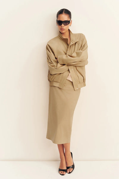 Front view of a model leaning against a wall with arms crossed wearing the unbuttoned Shona Joy Ernest sand faux suede jacket revealing inner press stud closures.