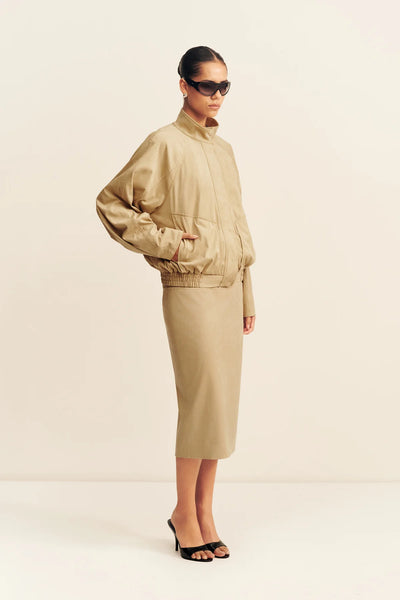 Three-quarter side angle showing a model wearing the sand Shona Joy Ernest bomber jacket with one hand in the pocket, highlighting the soft drape and side pocket design.