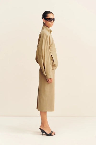 Side profile view of a model wearing the Shona Joy Ernest faux suede bomber jacket in sand paired with a matching column midi skirt and black heels.