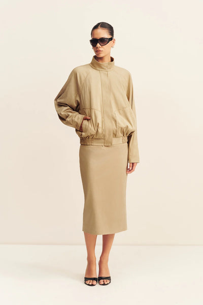 Three-quarter front view of a model posing with hands in pockets wearing the Shona Joy Ernest sand faux suede bomber jacket and matching skirt.