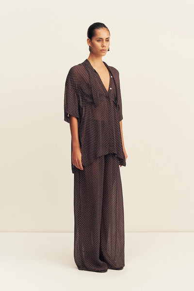 A full-length front studio shot of a model wearing the neck tie shirt styled open over a dark bralette, showcasing its relaxed, fluid fit designed to sit away from the body.