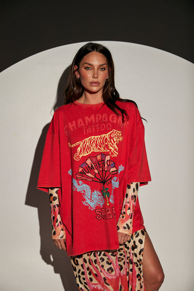 Front half-body view of a model wearing the bright red SABBI Very Oversized Champagne Tattoo Tee showcasing the yellow tiger, red fan, and blue dragon vintage tattoo artwork.