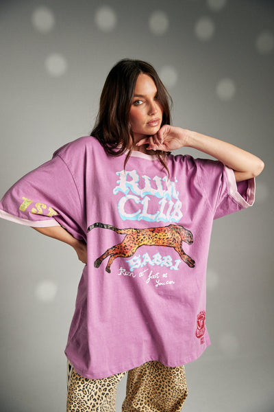 A close-up lifestyle portrait from the front showing a model adjusting her hair, detailing the comfortable fit around the neck and the graphic grunge chaos print elements across the chest.