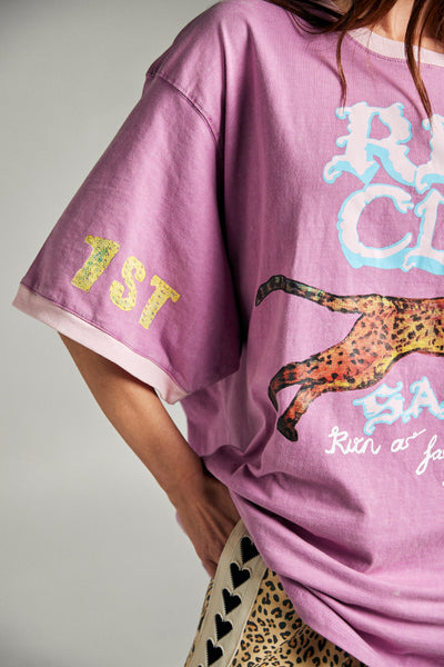 A close-up lifestyle portrait from the front showing a model adjusting her hair, detailing the comfortable fit around the neck and the graphic grunge chaos print elements across the chest.