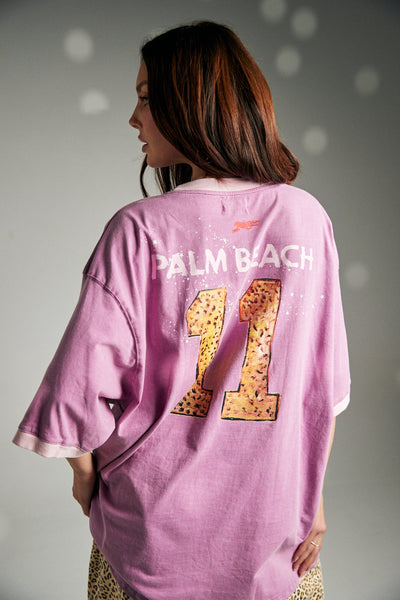 A side-angle outdoor campaign shot isolating the pink graphic jersey on a model, emphasizing the casual, slouchy sleeve drape and the sporty green striped taping detail along the sleeve cuffs.
