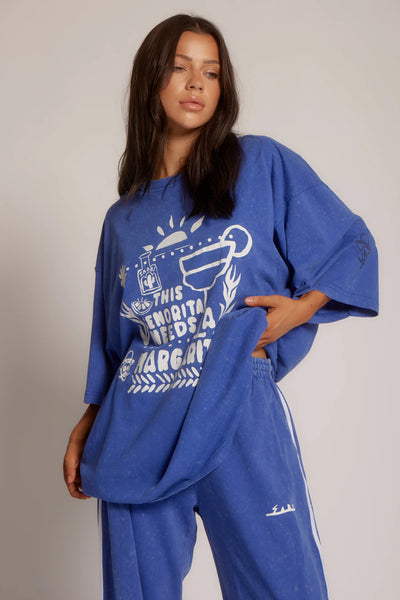 Three-quarter front view of a model holding the hem of Sabbi The Very Oversized Margie Tee in Royal Blue, highlighting the relaxed fit and sleeve graphic.