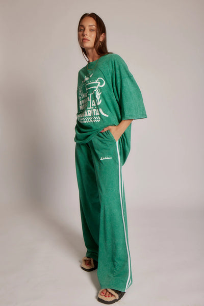 Full-length view of a model wearing Sabbi The Very Oversized Margie Tee in Forest Green paired with matching green track pants and slides.