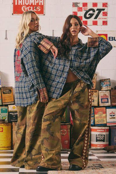 A full-length back view of the camo canvas pants on a model, illustrating the clean drape across the seat and the slouchy width down to the bottom hems.