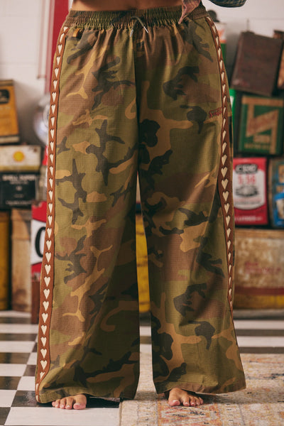 A full-length front studio shot of a model wearing SABBI The Canvas Heart Pants in Camo, highlighting the wide, relaxed leg profile and structured silhouette of the washed cotton canvas drill fabric.