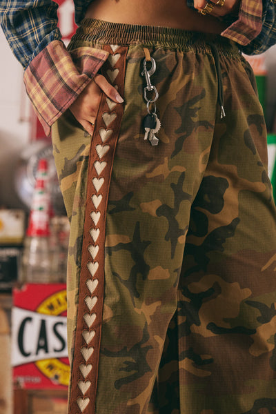 A side profile studio shot capturing the prominent brown woven heart taping running vertically down the full length of the leg seam.