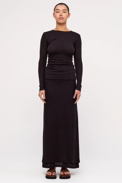 Full-length front view of a model wearing the lightweight Zulu & Zephyr Rib Hemp Jersey Long Sleeve Top in black, paired with a matching black skirt and brown open-toe platform shoes.