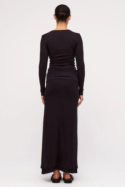 Full-length back view of a model wearing the Zulu & Zephyr Rib Hemp Jersey Long Sleeve Top and matching long skirt in black, paired with brown platform sandals.