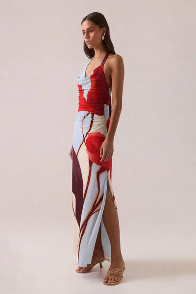 Three-quarter side profile view of a model in the Vere Kalea Blue Bloom halter maxi dress showcasing the asymmetric cowl neckline, side gathering, and high leg split.