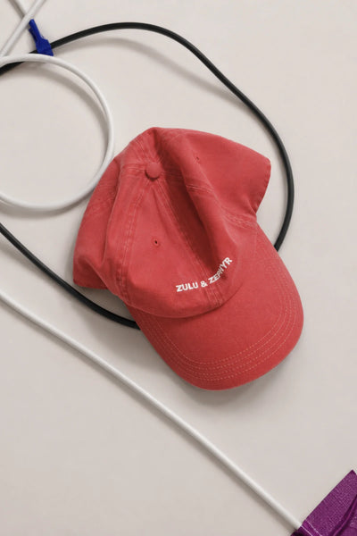 Overhead flat lay of the washed red Zulu & Zephyr Canvas Cap with white embroidered logo detailing on a neutral background with studio cables.