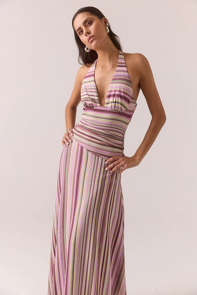 Three-quarter front view of a model posing in the Vere Sarina orchid halter maxi dress with a deep V-neckline, gathered waist, and vertical multi-color stripes.