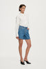 Studio side profile view of a model wearing the blue denim shorts and white shirt, highlighting the wide leg opening and mid-thigh length.