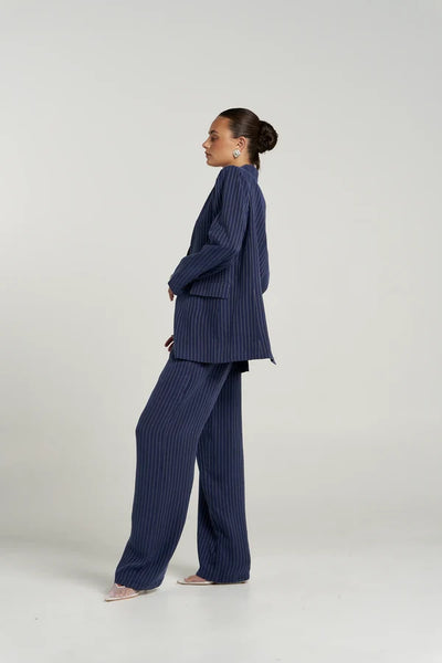Front detail view of model wearing the Summi Summi Boss Pant in Navy Pinstripe, showing the mid-waist waistband, belt loops, and relaxed wide-leg cut.