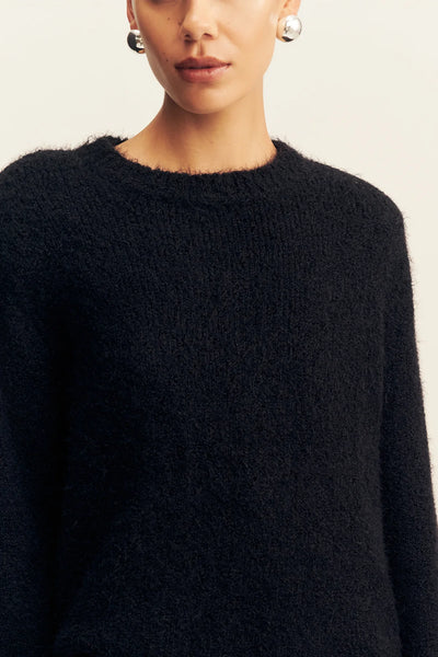 Close-up portrait of a model highlighting the plush texture, round ribbed collar, and structured shoulder shape of the black Shona Joy Korine boucle knit sweater.