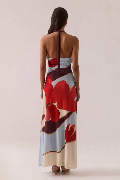 Full-length back view of a model wearing the Vere Kalea halter neck maxi dress in Blue Bloom featuring an open back, neck tie detail, and large floral placement print.