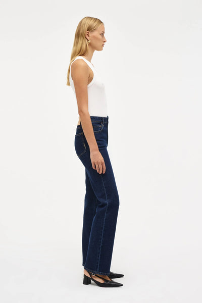 Full-length side profile studio shot of a model wearing the mid-rise Freja Straight jeans and a white tank top. The image showcases the streamlined, timeless straight-leg silhouette from the hip down to the hem.