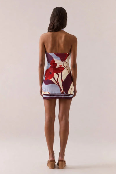 Full-length back view of a model wearing the Vere Kalea halter mini dress in Blue Bloom showcasing an open back and bold floral placement print.