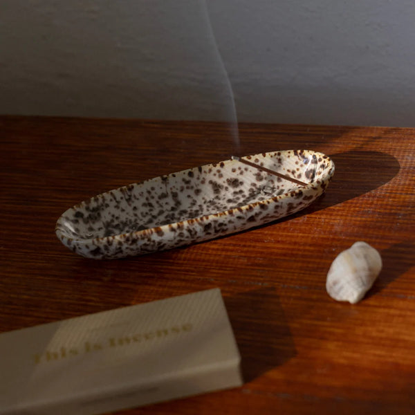Elevated lifestyle view of the Gentle Habits Collector Ceramic Incense Holder in Leopard print holding a burning incense stick alongside a box of This Is Incense on a warm wooden surface.