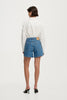Full-length studio rear view of a model wearing the high-rise denim shorts and a white button-down shirt, highlighting the back pockets and tailored fit.