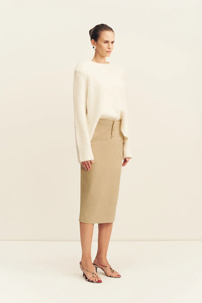 Three-quarter view of a model wearing the snow white Shona Joy Korine shoulder-padded boucle knit jumper tucked into a button-front sand midi skirt.