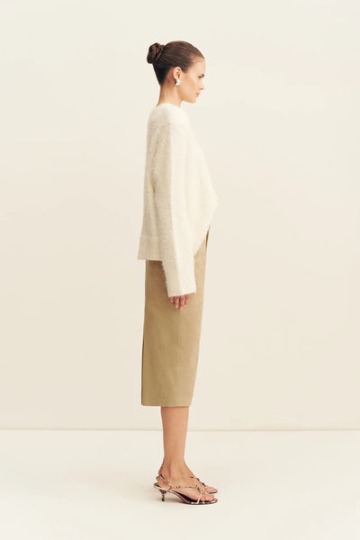 Side profile view of a model wearing the snow white Shona Joy Korine oversized boucle knit sweater styled with a sand column midi skirt and patterned heels.