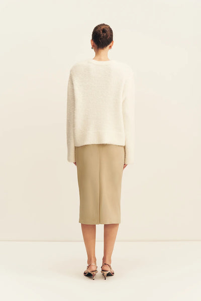 Rear full-length view of a model wearing the snow white Shona Joy Korine fluffy boucle knit sweater paired with a high-waisted sand midi skirt.