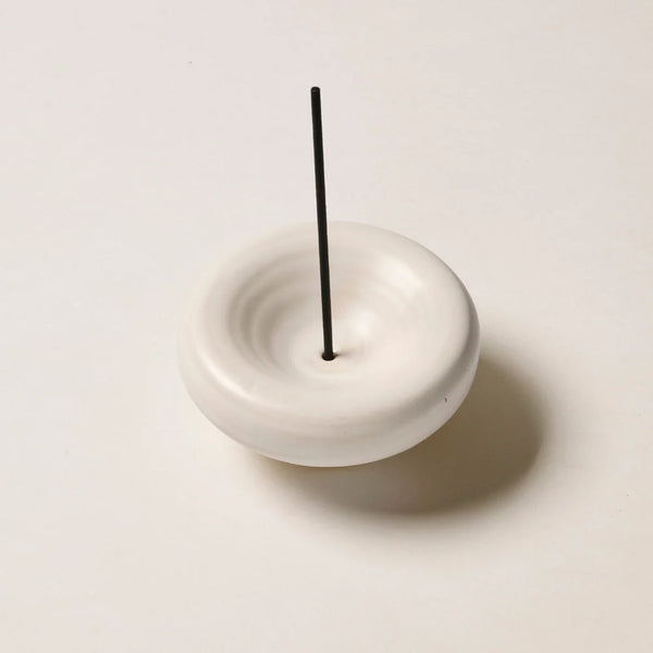 Studio shot of the Gentle Habits Vessel Incense Holder in Cream with a single black incense stick placed upright in the center opening on a neutral off-white surface.
