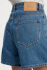 Close-up rear view of the blue denim shorts, showcasing the tan Neuw leather brand patch on the waistband, pocket stitching, and signature repair stitch detail.