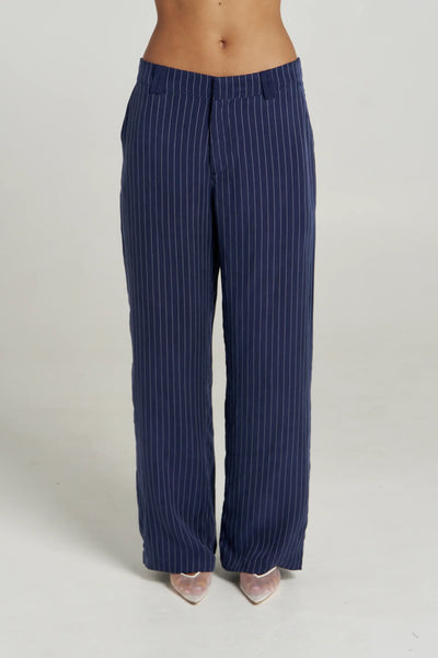 Editorial crouching studio shot of model wearing the Summi Summi Navy Pinstripe Boss Pant set with matching long-sleeve collared shirt and silver chain necklace.