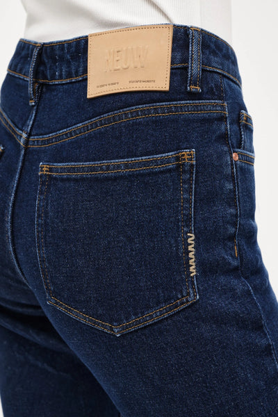 A close-up, back-angle shot of the Freja Straight in Paris. The image showcases the signature tan leather Neuw brand patch on the waistband, the clean back pocket structure, and the brand's subtle signature repair stitch details along the side of the back pocket.