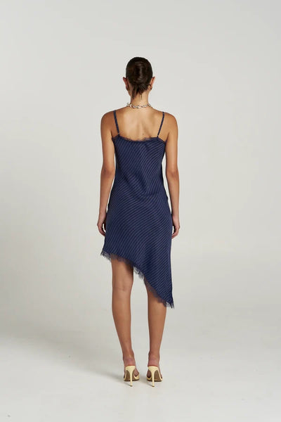 Back view of model wearing the Summi Summi Asym Siren Dress in Navy Pinstripe, displaying the straight lace-trimmed back neckline, adjustable straps, and slanted hemline.