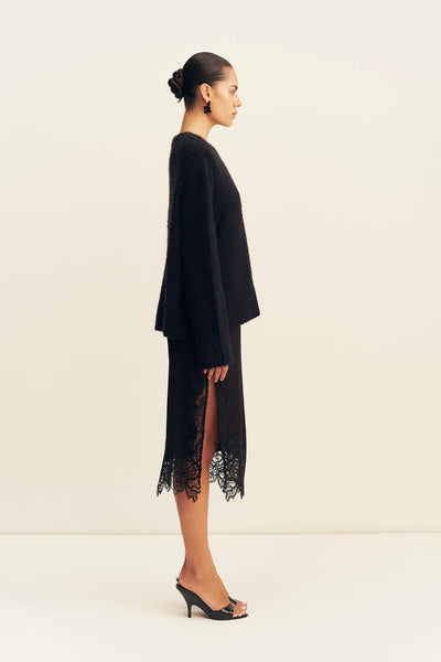 Side profile view of a model wearing the black oversized Shona Joy Korine boucle knit sweater layered over a black lace split midi skirt.