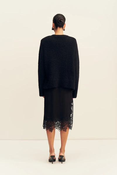 Back view of a model wearing the relaxed black Shona Joy Korine fluffy boucle sweater paired with a lace-trimmed black midi skirt and heels.