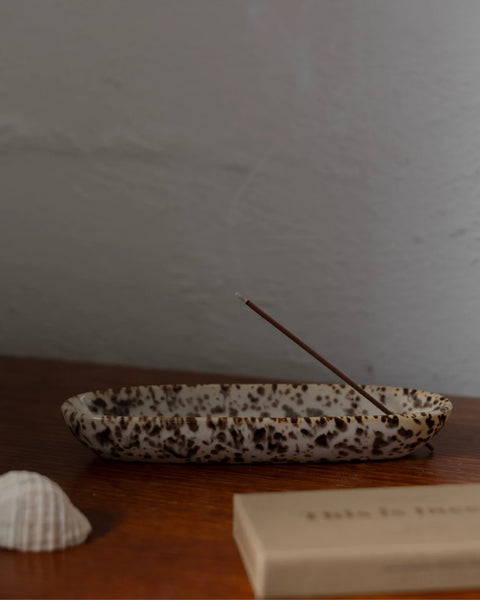 Side profile shot of the Gentle Habits Collector Ceramic Holder in Leopard glaze, resting on a wooden table with a lit burning incense stick and a seashell accessory.