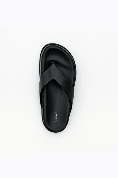 Top-down view of the black leather Wallace sandal, showing the rounded toe, wide thong strap, and the "ALIAS MAE" brand logo printed on the insole.