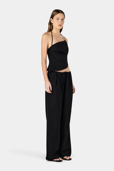 Studio three-quarter front view of a model wearing relaxed black straight-leg trousers with a waist drawcord and an asymmetrical top.