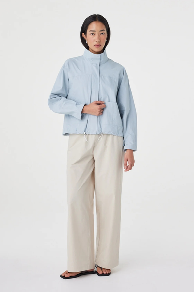 Full-length studio front shot of a model wearing the pale blue Arcaa Movement Addie Jacket paired with wide-leg cream trousers and black flat thong sandals.