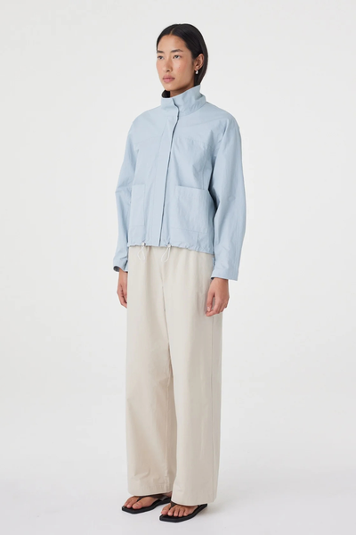 Three-quarter studio view of a model wearing the pale blue Arcaa Movement Addie Jacket showing the relaxed fit, long sleeves, and funnel neck closure.