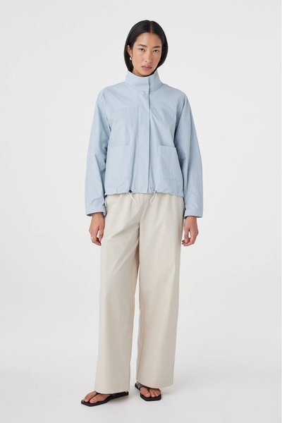 Full-length studio front pose of a model wearing the pale blue Arcaa Movement Addie Jacket and wide-leg neutral trousers against a plain white background.