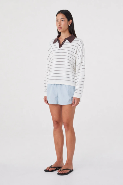 Three-quarter side studio view of a model in the pale blue Arcaa Movement Addie Short paired with a striped collared top and flat black thong sandals.