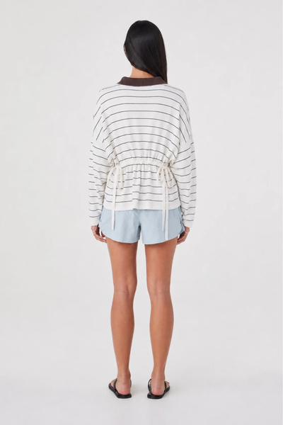 Full-length studio back view of a model wearing the pale blue Arcaa Movement Addie Short and a white striped long-sleeve top with back waist ties.