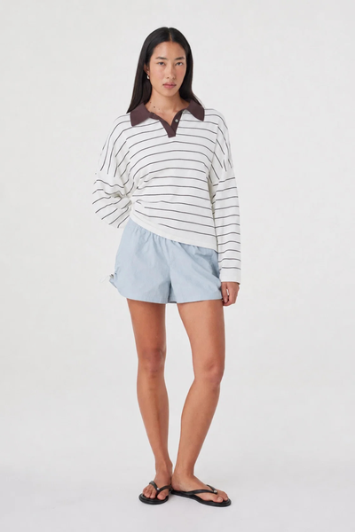 Full-length studio pose of a model wearing the pale blue Arcaa Movement Addie Short with one hand placed behind her back, paired with a striped pullover.